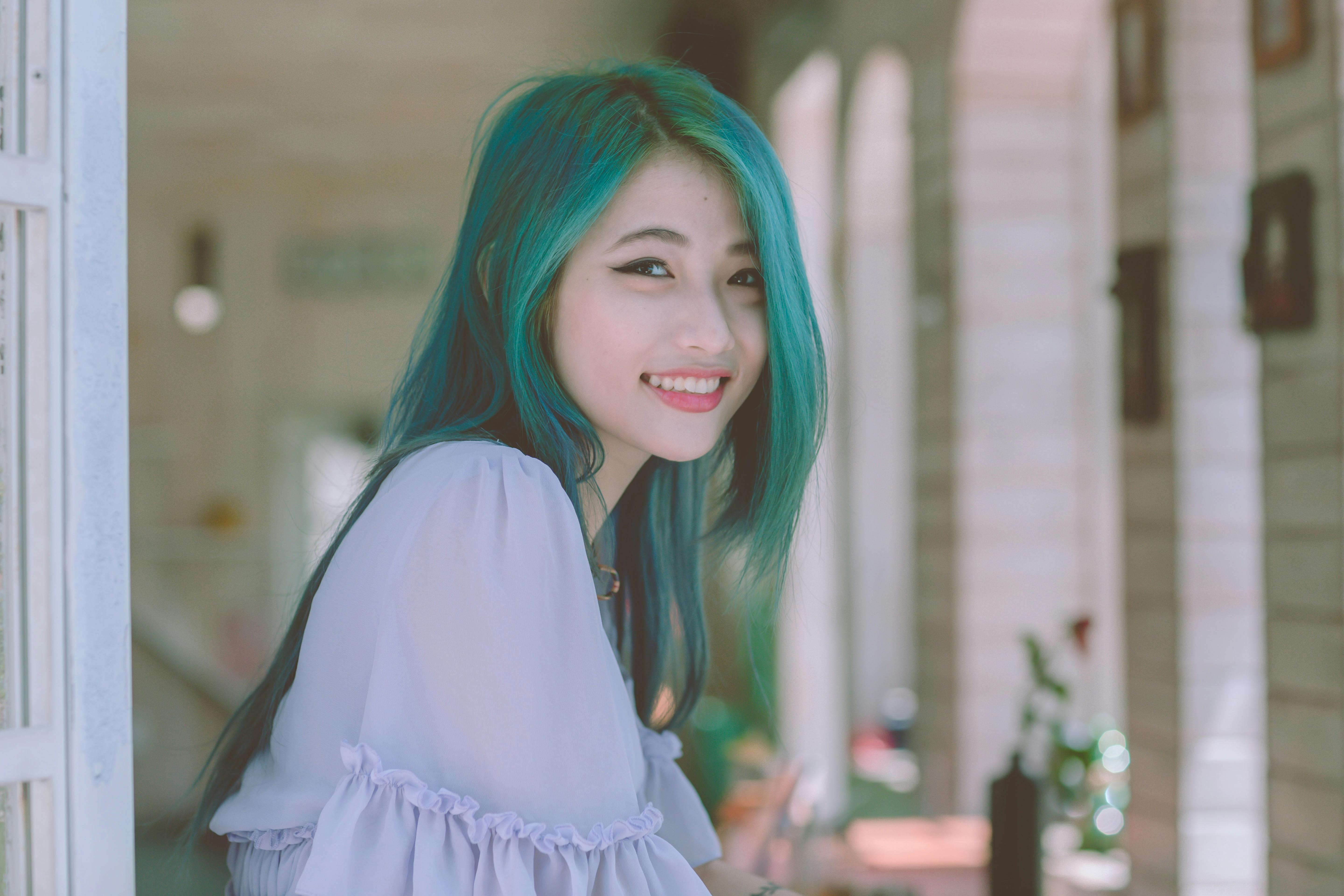 Beautiful young woman with vibrant green hair smiling happily indoors.